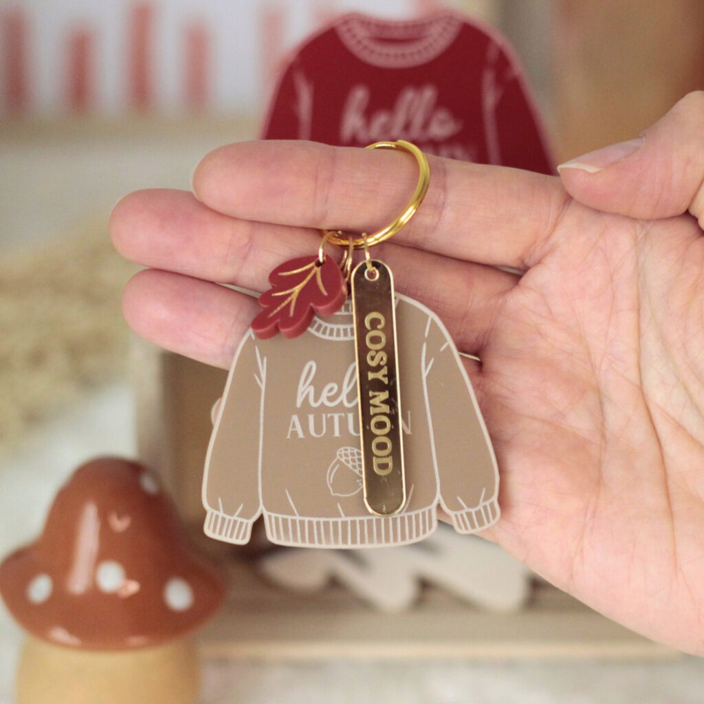 Porte-clé pull Hello Autumn moka présenté à la main avec languette personnalisée en miroir doré